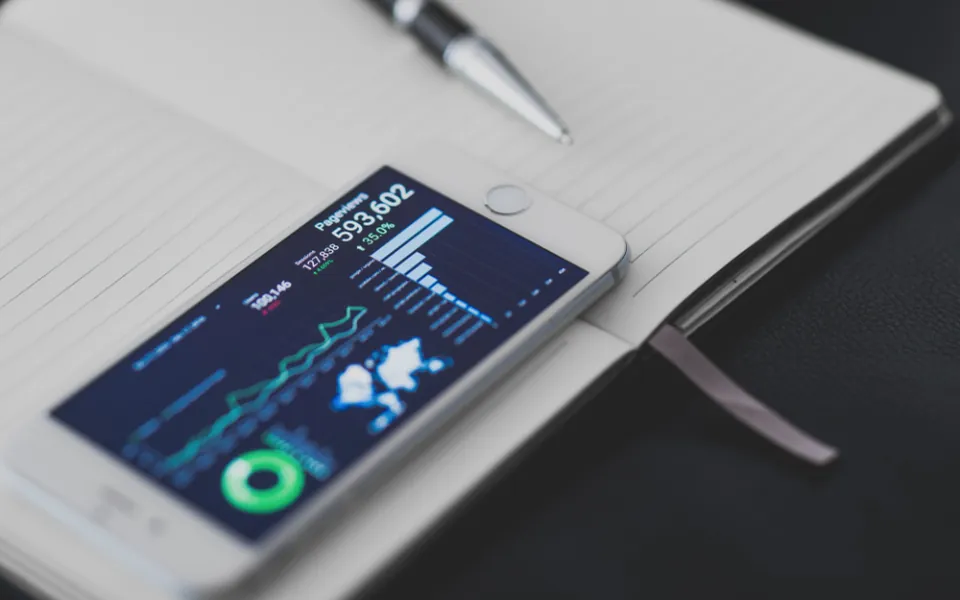Smartphone showing a data dashboard next to a notebook, representing AI agents automating tasks