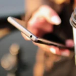Person holding a smartphone and a coffee cup, checking for software updates