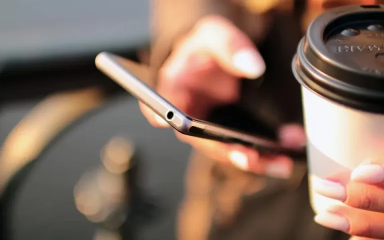 Person holding a smartphone and a coffee cup, checking for software updates